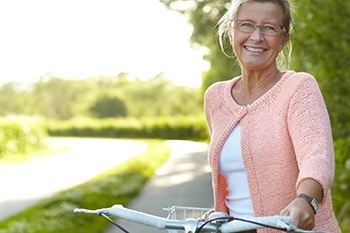 Senior woman with dental implants smiling outdoors, holding bicycle
