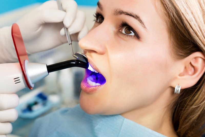a dentist using a curing light on a female patient’s tooth to harden the composite resin