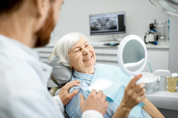 older woman admiring smile in mirror at dentist's office
