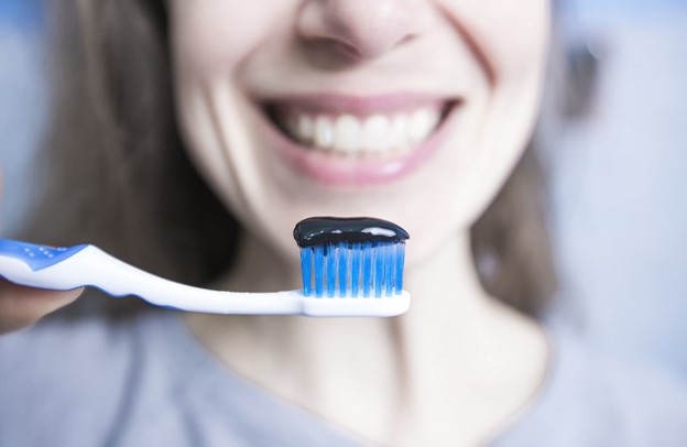Woman holding toothbrush with charcoal toothpaste.