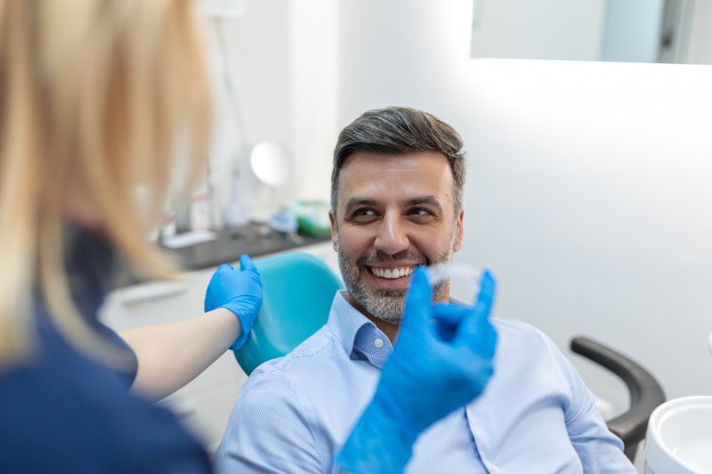 A young dentist holding an Invisalign tray in front of a patient 