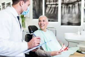 Older woman with white hair in dental chair smiling at dentist 